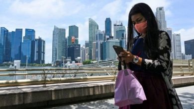 امرأة مستغرقة في تفحص هاتفها المحمول أمام عدد من ناطحات السحاب في سنغافورة